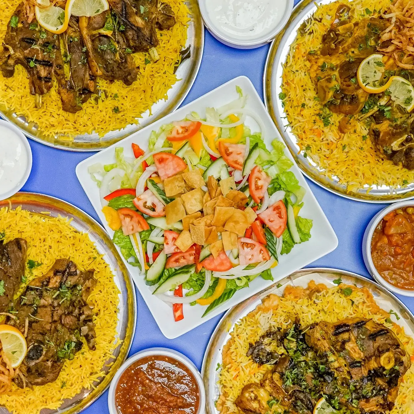 Overhead view of madhbi lamb platters over golden rice with a fresh house salad at the centre.