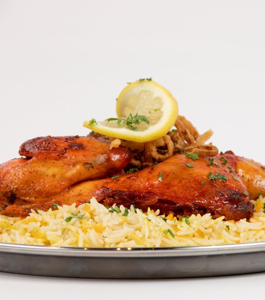 Our chicken mandi — steam-roasted chicken over saffron basmati, topped with crispy onions and lemon.