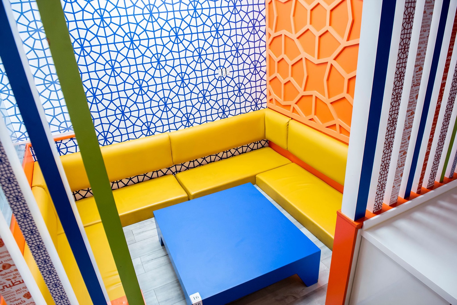 The majlis corner of our East York dining room — cobalt girih-tile wallpaper, orange honeycomb screens and sunny yellow booths.