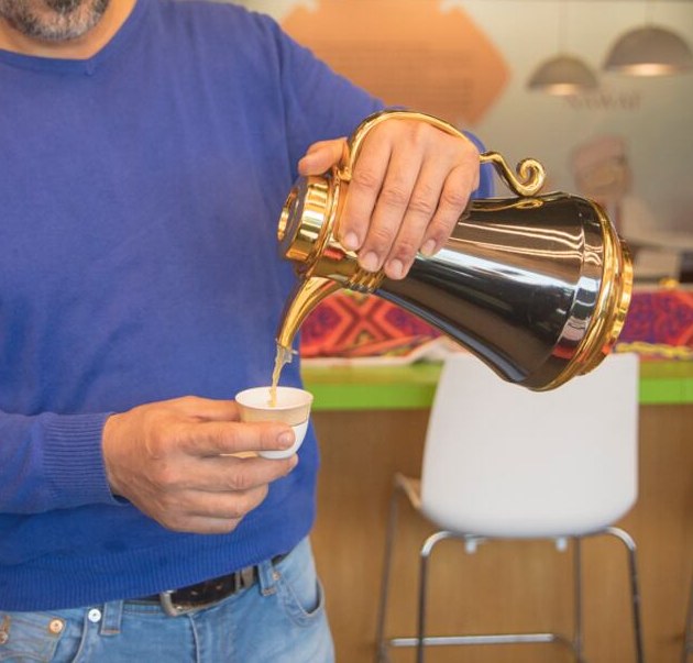 Fresh Arabic coffee poured from a golden dallah into a small finjan at our counter.